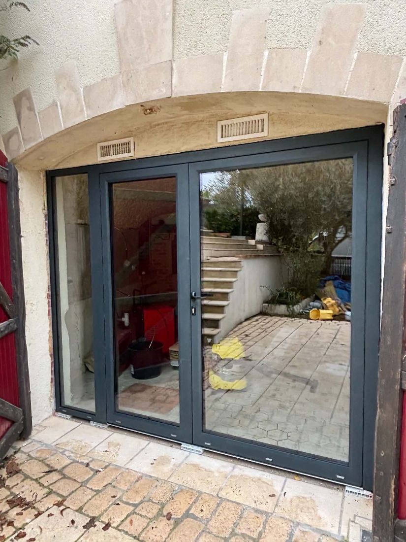 Baie vitrée en aluminium gris anthracite ouvrant sur une cour pavée