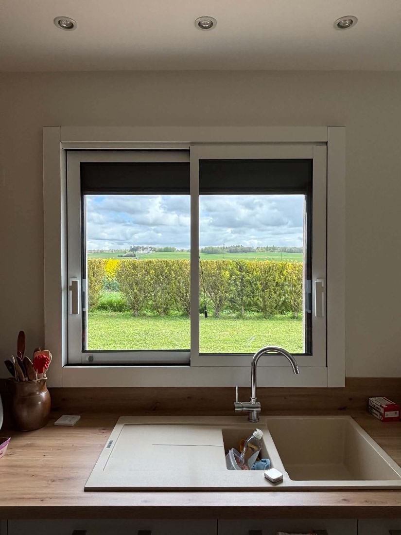 Fenêtre coulissante blanche au-dessus d’un évier, vue sur la campagne