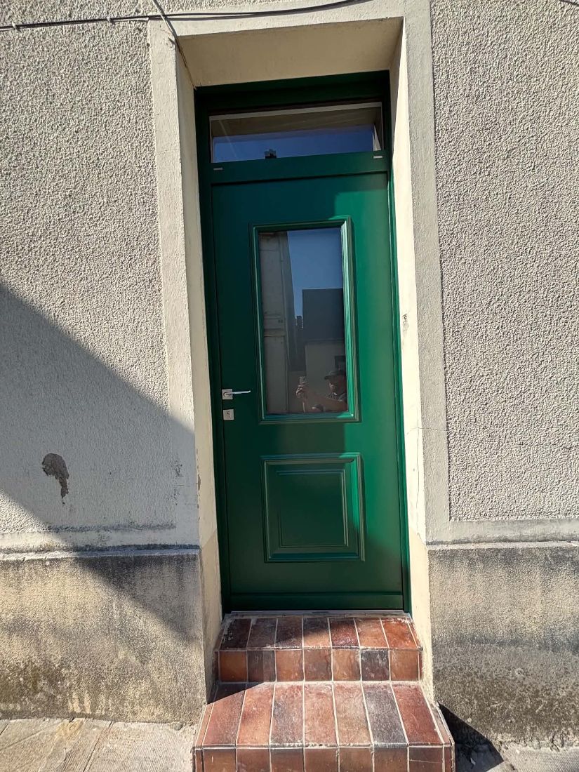 Porte d’entrée verte vitrée avec imposte, sur un perron en briques