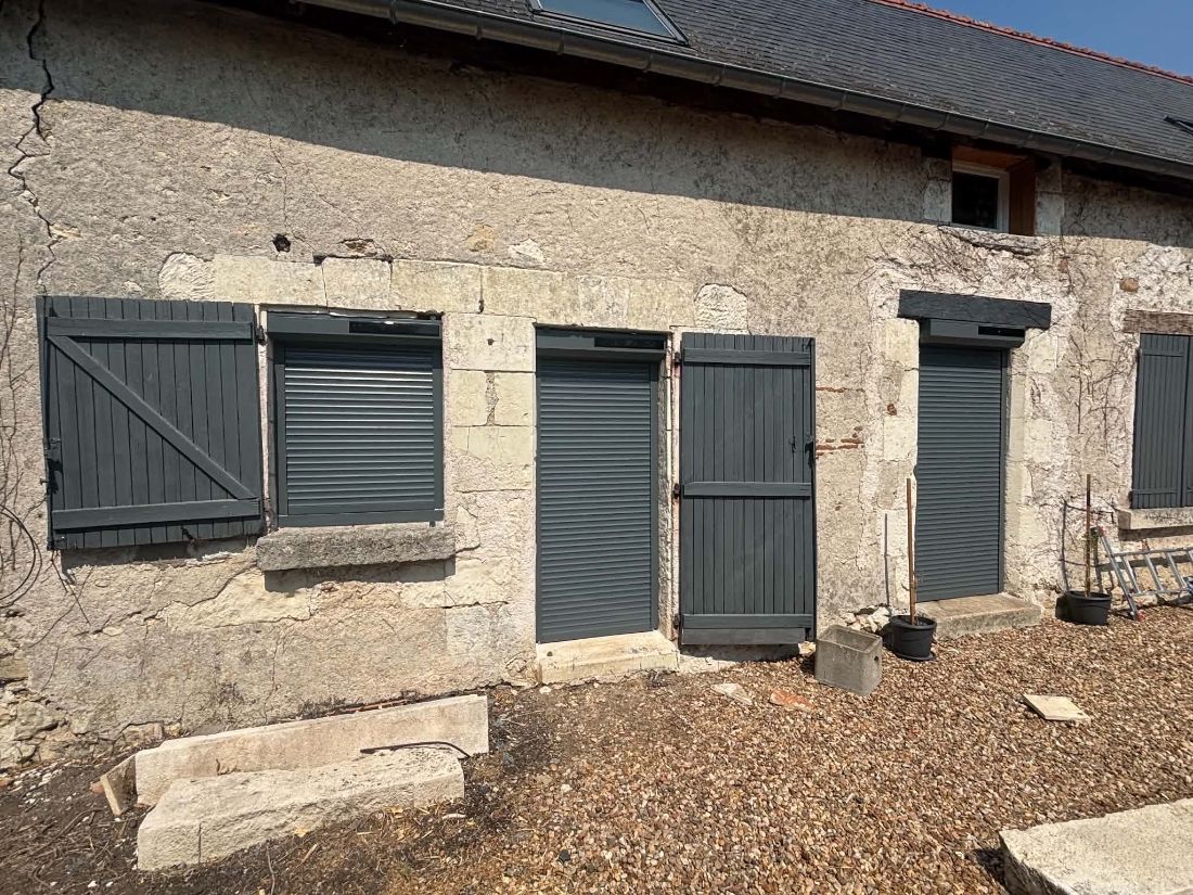Façade en pierre avec volets battants gris et volets roulants